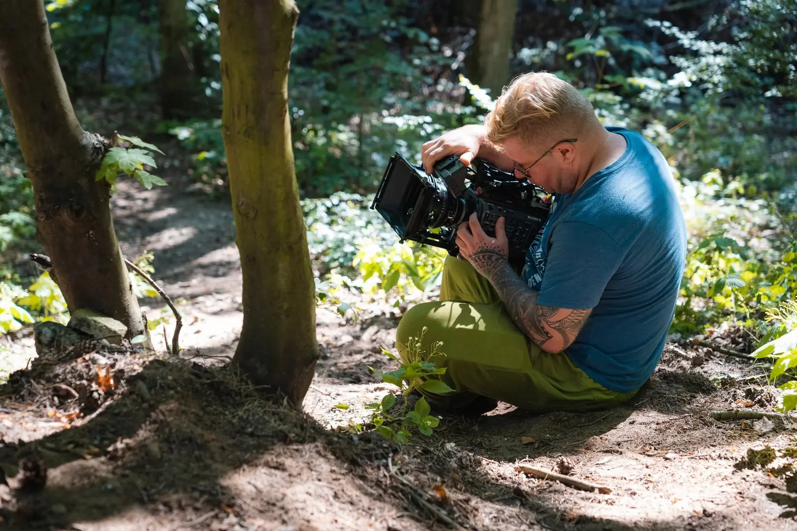Łukasz Nyks z kamerą filmową w lesie, na planie zdjęciowym